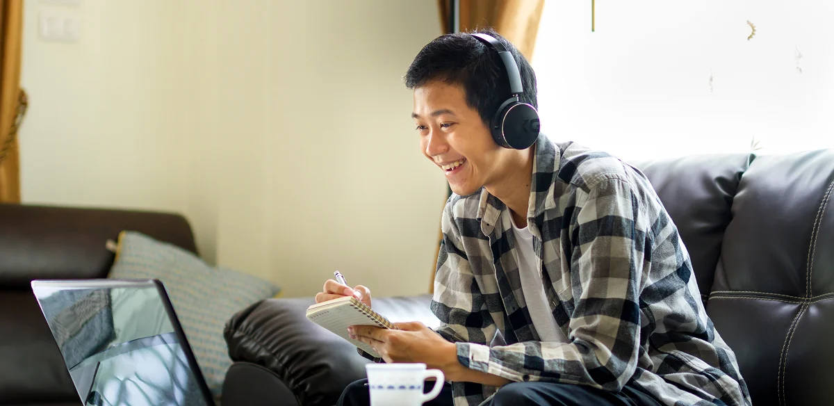 Student taking notes while taking an online class at home